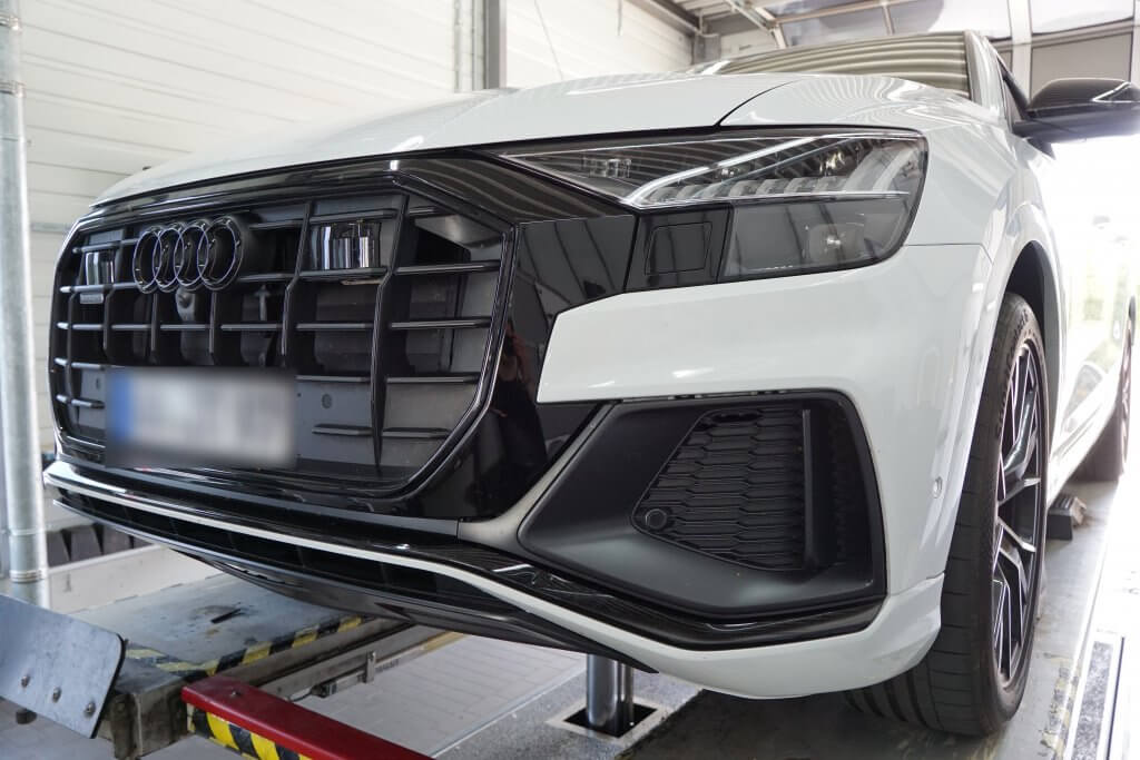 Ein weißer Audi SUV steht mit abgenommener Frontstoßstange auf einer Hebebühne in einer Werkstatt