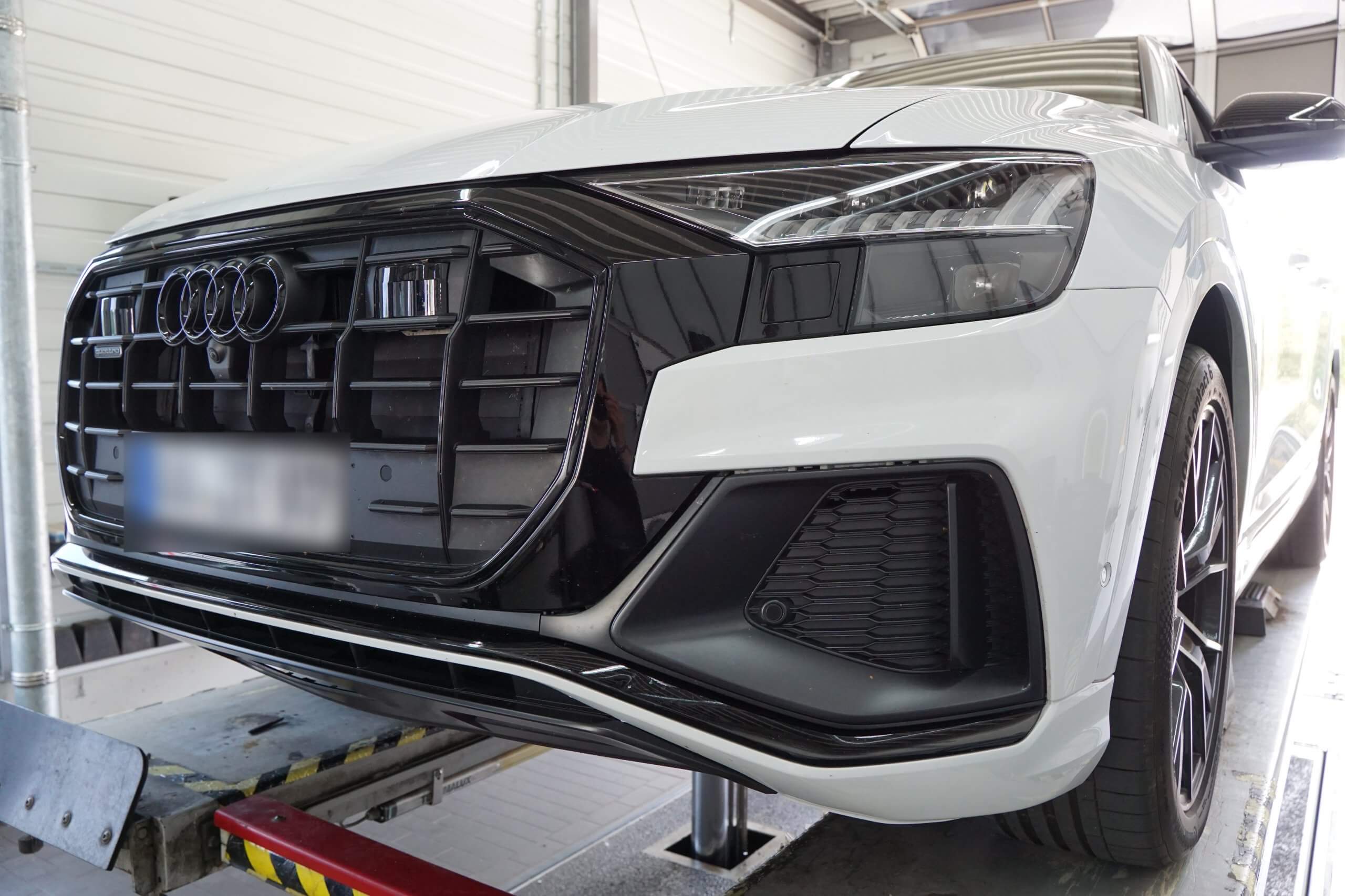 Ein weißer Audi SUV steht mit abgenommener Frontstoßstange auf einer Hebebühne in einer Werkstatt