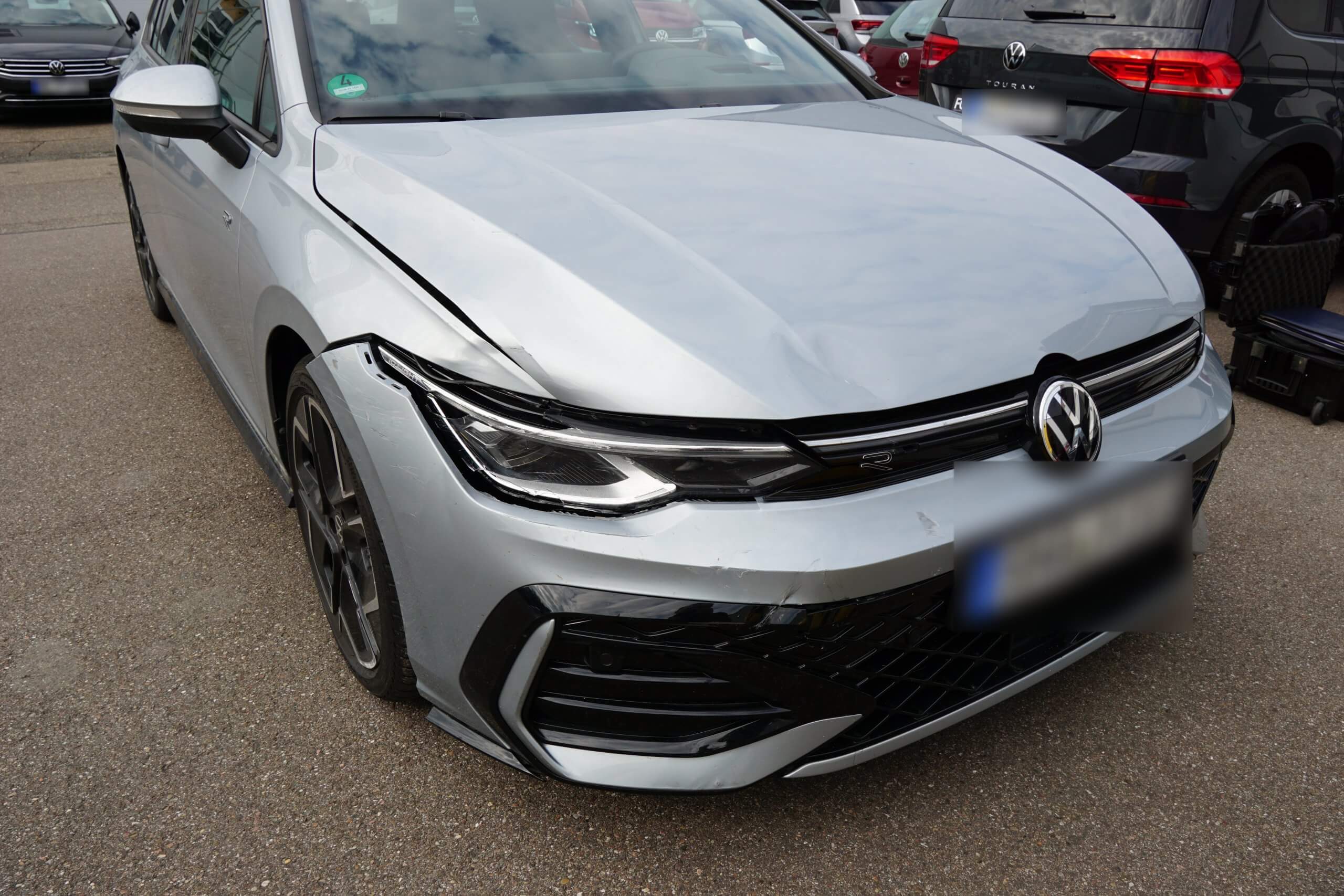 Ein silberner Volkswagen mit beschädigter Frontstoßstange und Motorhaube steht auf einem Parkplatz