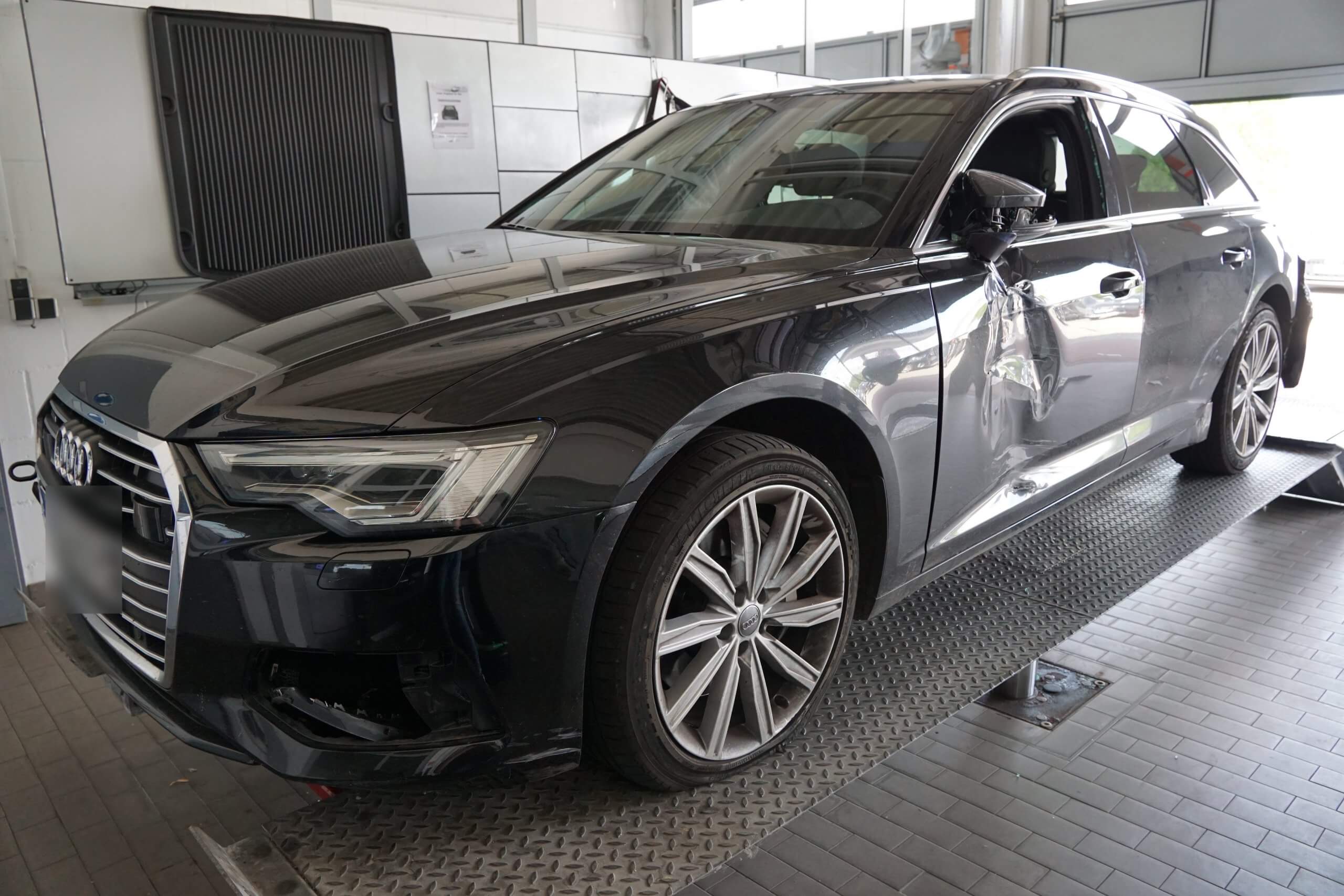 Ein dunkler Audi mit sichtbaren Seitenschäden steht auf einer Plattform in einer Werkstatt oder Autowerkstatt