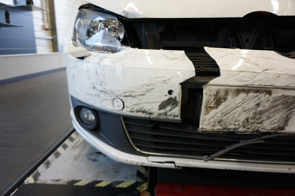 Nahaufnahme der vorderen Stoßstange eines Autos mit Dellen, Kratzern und Schäden am Scheinwerfer nach einem frischen Unfall