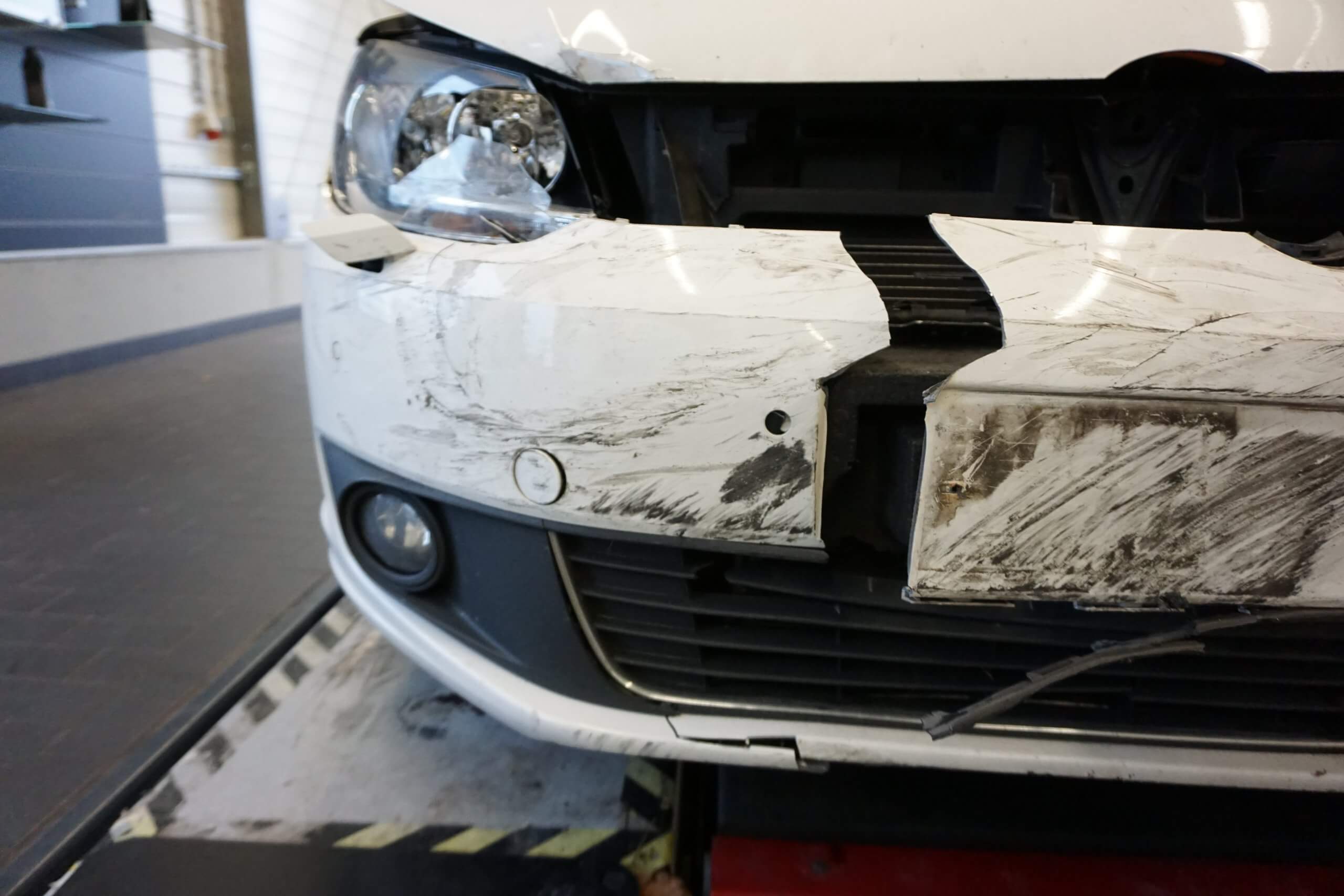 Nahaufnahme der vorderen Stoßstange eines Autos mit Dellen, Kratzern und Schäden am Scheinwerfer nach einem frischen Unfall
