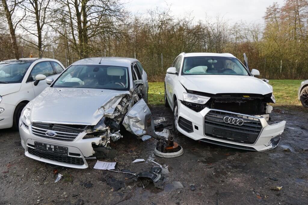 Zwei beschädigte silberne Autos, ein Ford und ein Audi, stehen nach einem Zusammenstoß nebeneinander, rundum liegen Trümmer