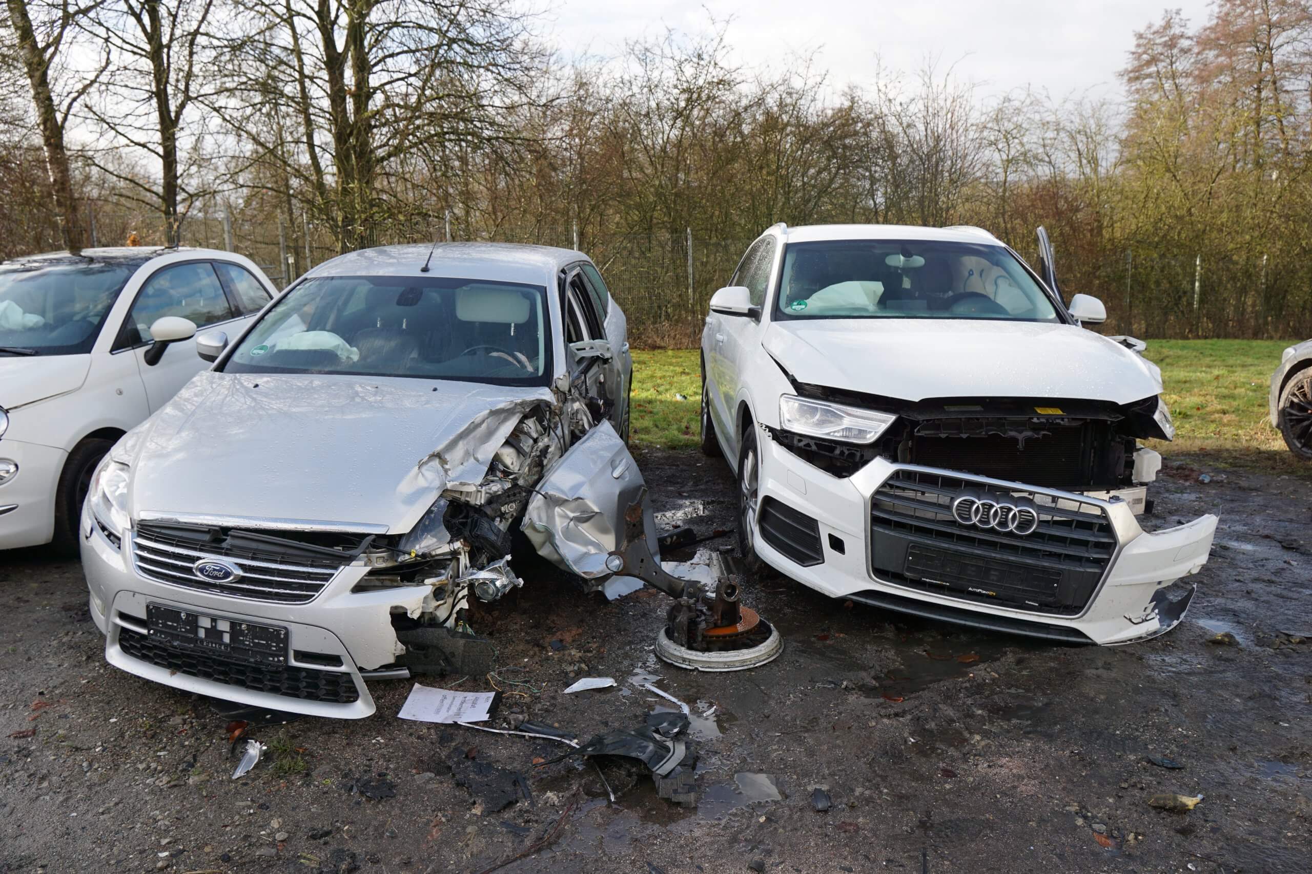 Zwei beschädigte silberne Autos, ein Ford und ein Audi, stehen nach einem Zusammenstoß nebeneinander, rundum liegen Trümmer