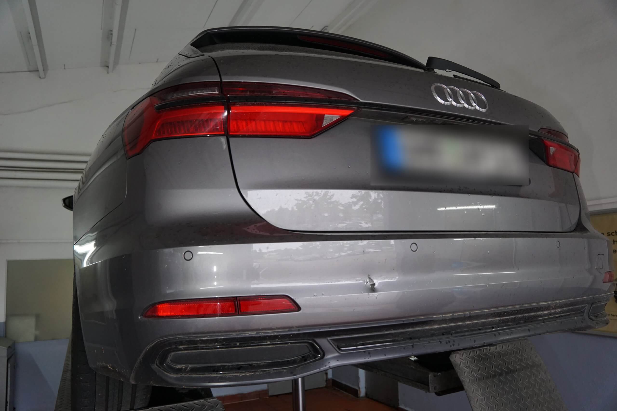 Ein grauer Audi mit einer Delle am hinteren Stoßfänger wird in einer Werkstatt zur Inspektion oder Reparatur angehoben