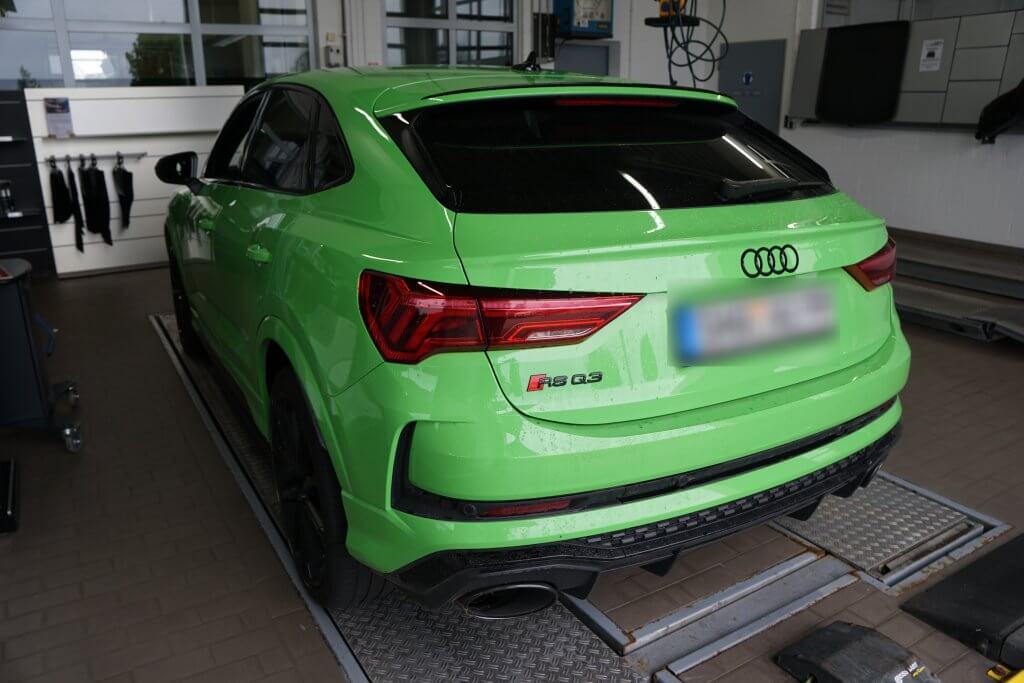 Ein knallgrüner Audi RS Q3 steht in einer Halle auf einer Hebebühne, aus schräger Rückansicht links betrachtet