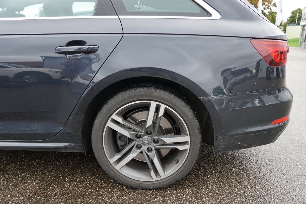 Nahaufnahme des Hinterrads und Seitenteils eines dunkelgrauen Autos auf nasser Straße, gut geeignet zur Dokumentation für ein Unfallgutachten