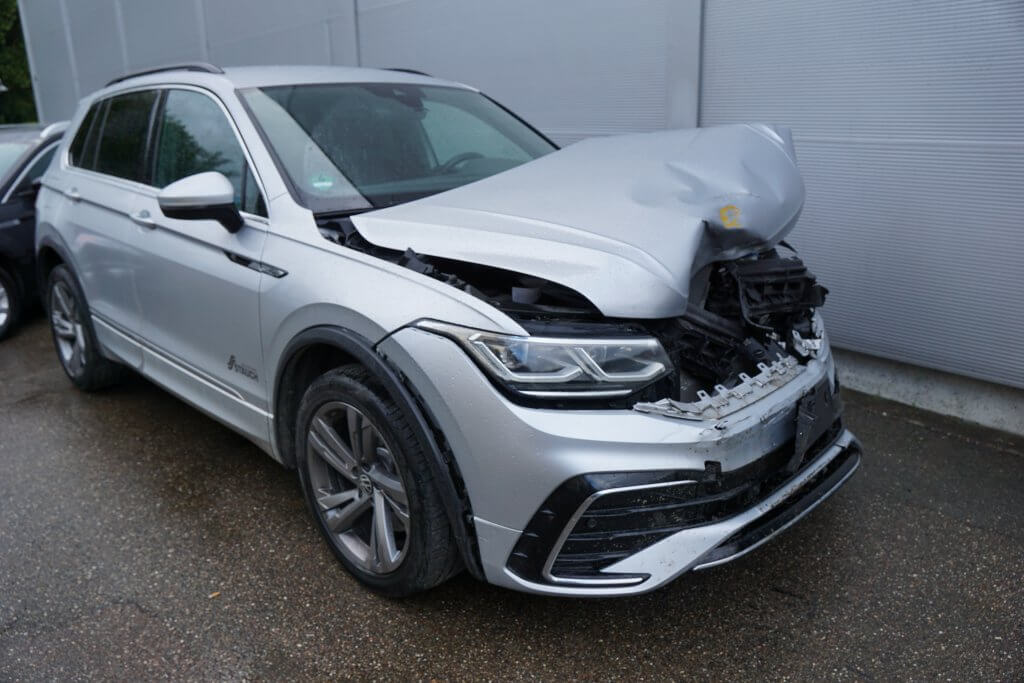 Ein silberner SUV mit starkem Frontschaden steht für einen Kostenvoranschlag auf einer nassen Straße nahe einer Hauswand