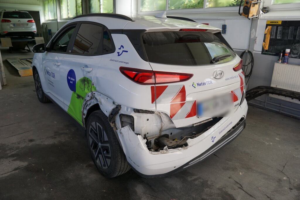 Ein weißer Hyundai SUV mit Firmenlogos und Heckschaden steht zur Reparatur in einer Werkstatt