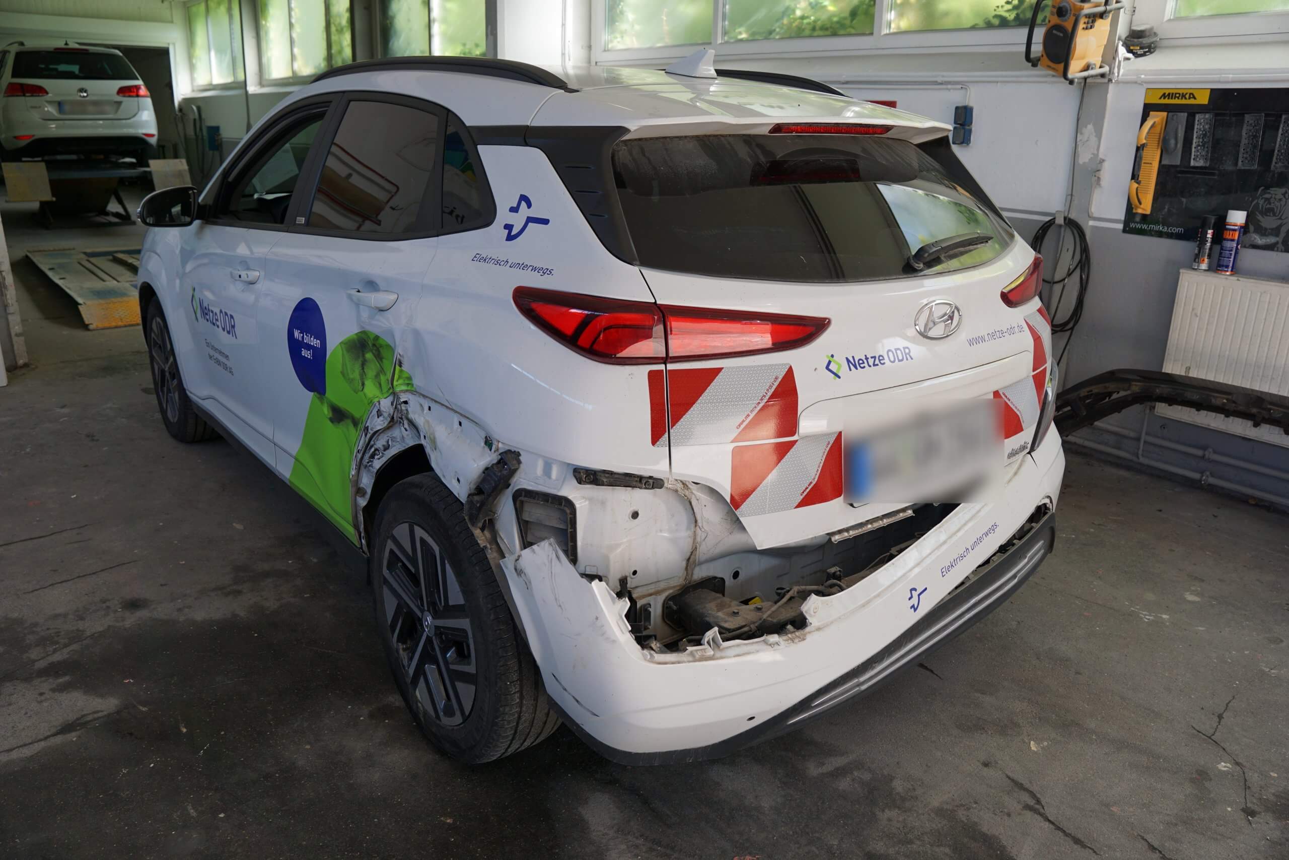 Ein weißer Hyundai SUV mit Firmenlogos und Heckschaden steht zur Reparatur in einer Werkstatt