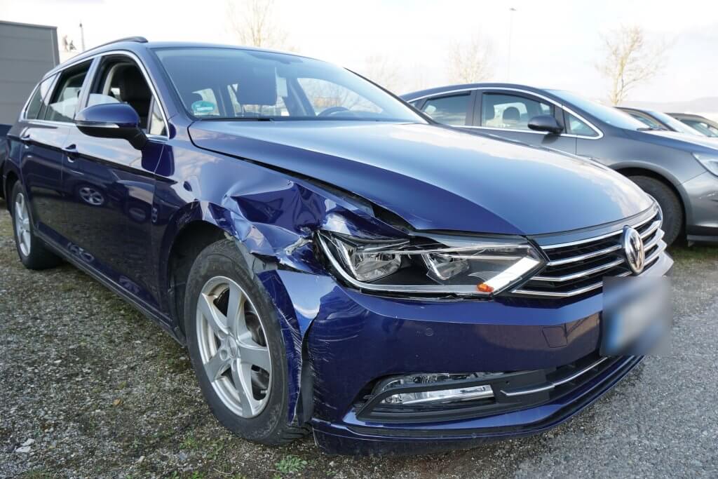 Ein blauer Volkswagen mit sichtbarem Schaden vorne links steht neben einem weiteren Auto