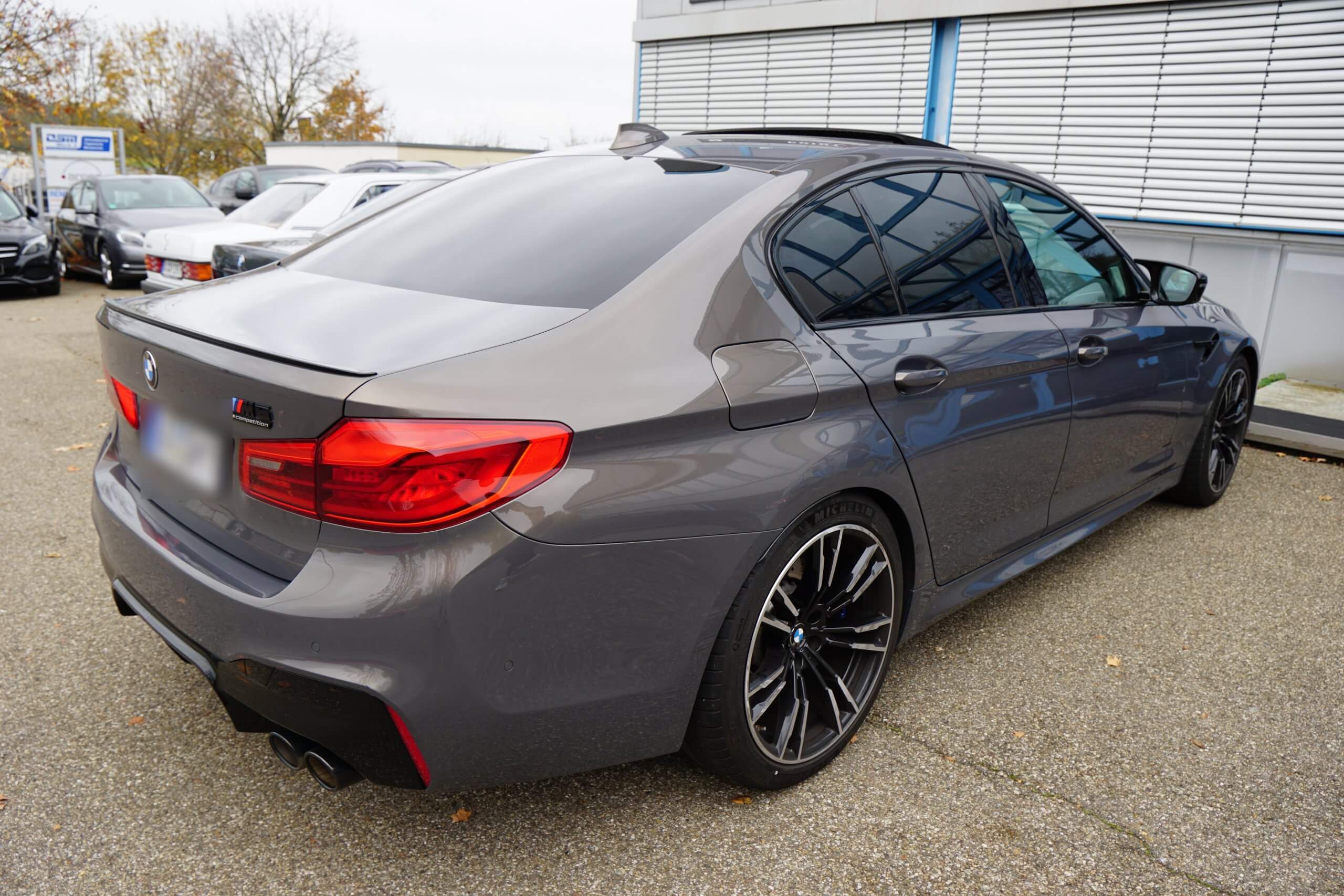 Ein grauer BMW M5 steht draußen und ist aus schräger Rückansicht von links zu sehen