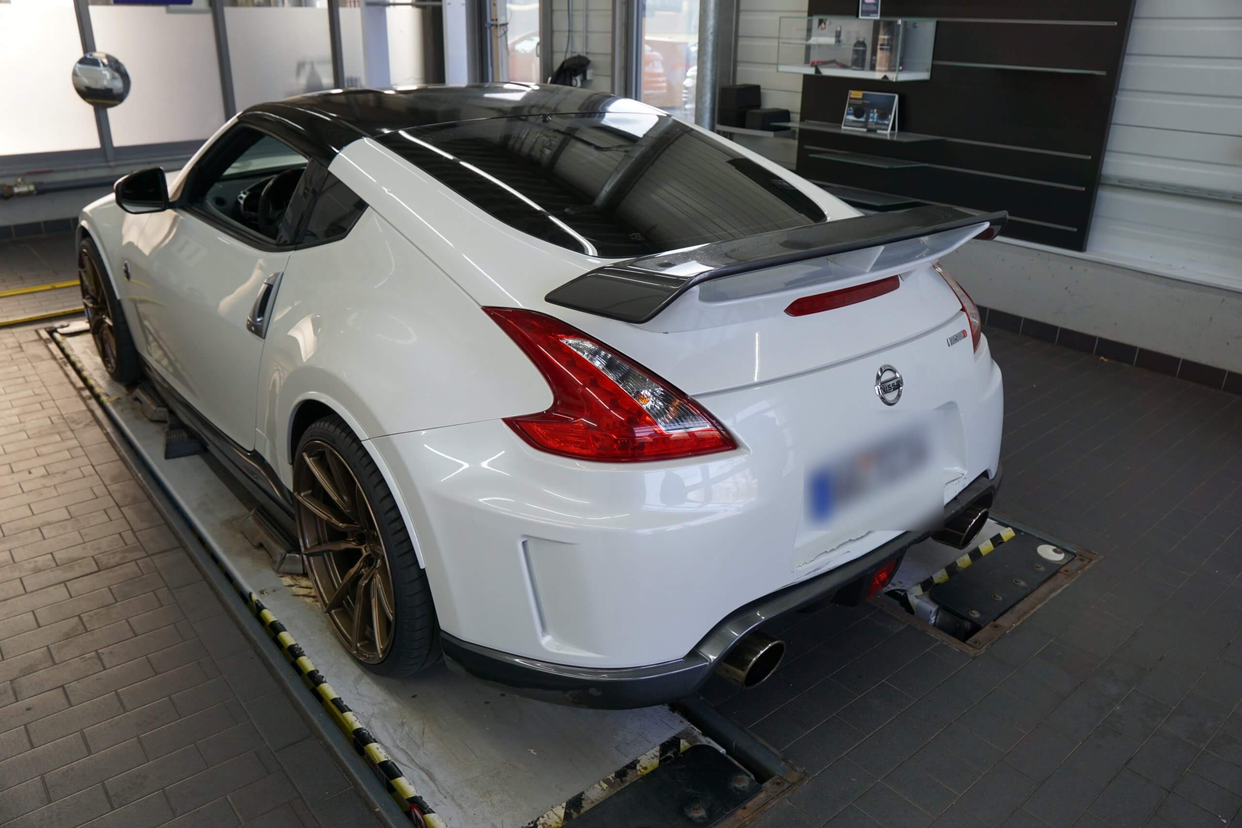 Ein weißer Nissan Sportwagen mit Heckspoiler steht auf einer Hebebühne in einer Werkstatt
