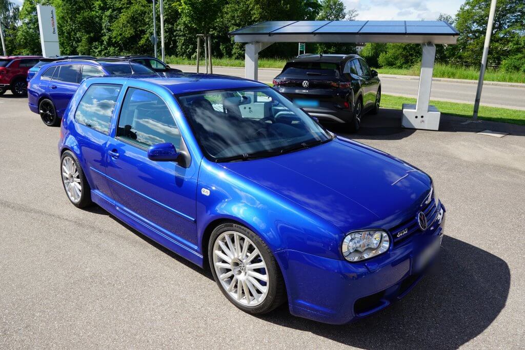 Ein leuchtend blauer VW Golf für ein Wertgutachten steht auf einem gepflasterten Parkplatz, umgeben von anderen Autos und Grünflächen