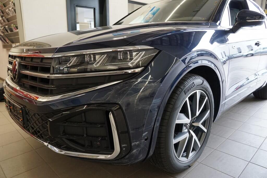 Nahaufnahme eines dunkelblauen Volkswagen SUV mit Scheinwerfer, Kühlergrill und Rad, ideal für den nächsten Kostenvoranschlag