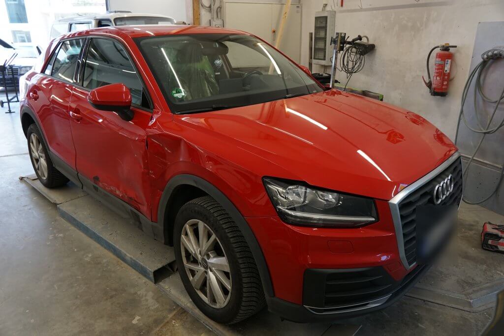 Ein roter Audi SUV mit sichtbaren Schäden auf der linken Seite steht in einer Autowerkstatt