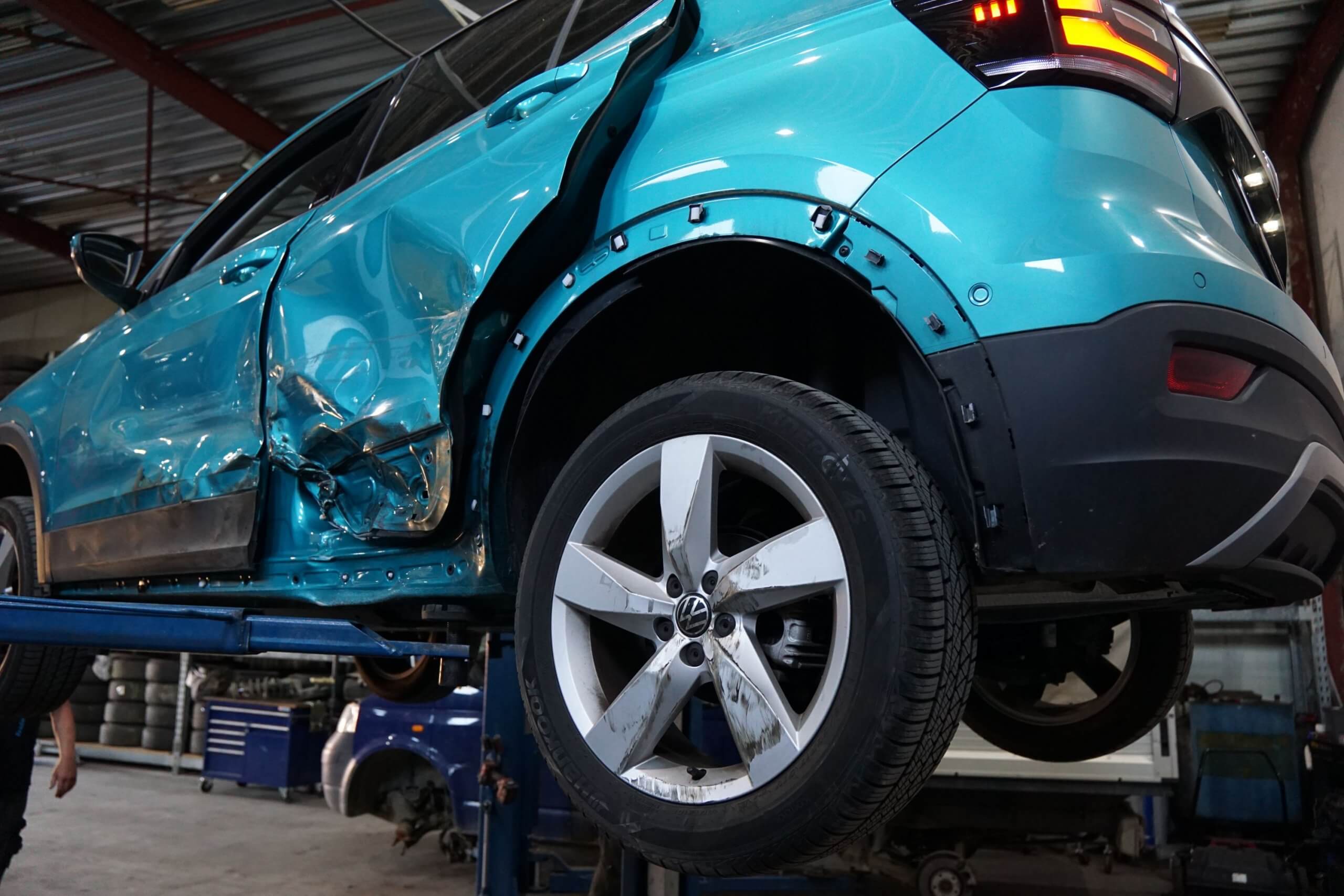 Ein blaues Auto mit schweren Seitenschäden wird in einer Autowerkstatt auf einer Hebebühne angehoben