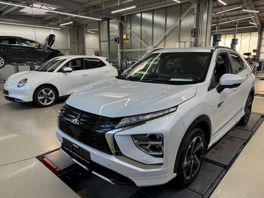 Zwei weiße SUVs stehen in einer hell erleuchteten Werkstatt, einer auf einer Hebebühne, der andere bereit zum Gebrauchtwagencheck