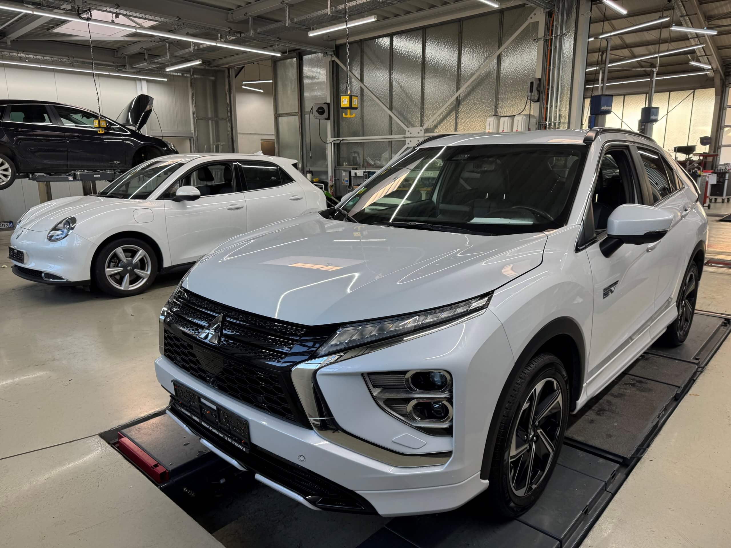 Zwei weiße SUVs stehen in einer hell erleuchteten Werkstatt, einer auf einer Hebebühne, der andere bereit zum Gebrauchtwagencheck